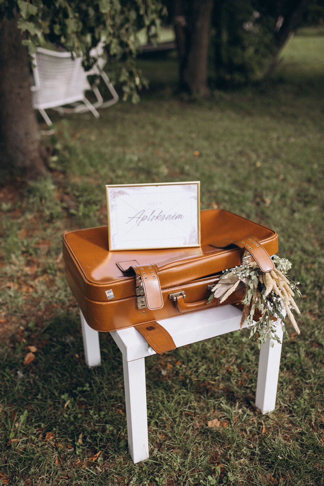 Brūns koferis, kas stāv uz balta galda ar kāzu dekorējumiem